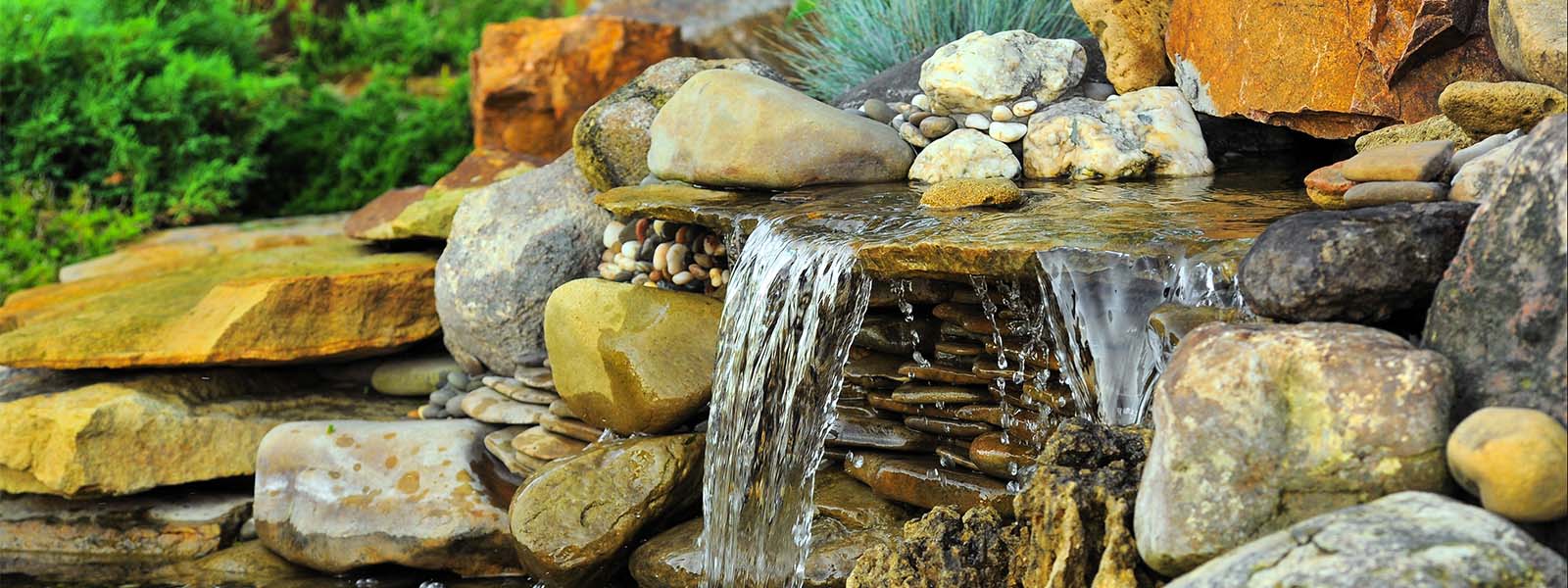 Stone waterfall with multicolored rocks and bushes in the background.
